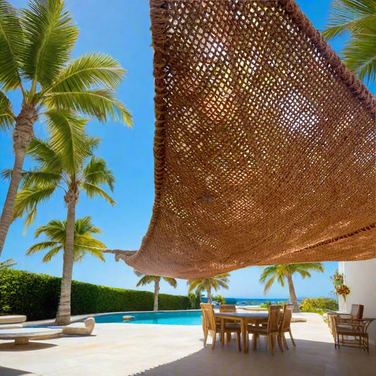 16ft elongated triangle coconut fiber shade sail creating sculptural shade over a poolside patio dining area with palm trees.