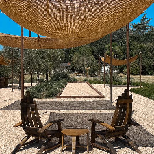 10ft x 13ft rectangle shade sail providing patio shade over a pair of wooden lounge chairs and outdoor table beside a bocce court.