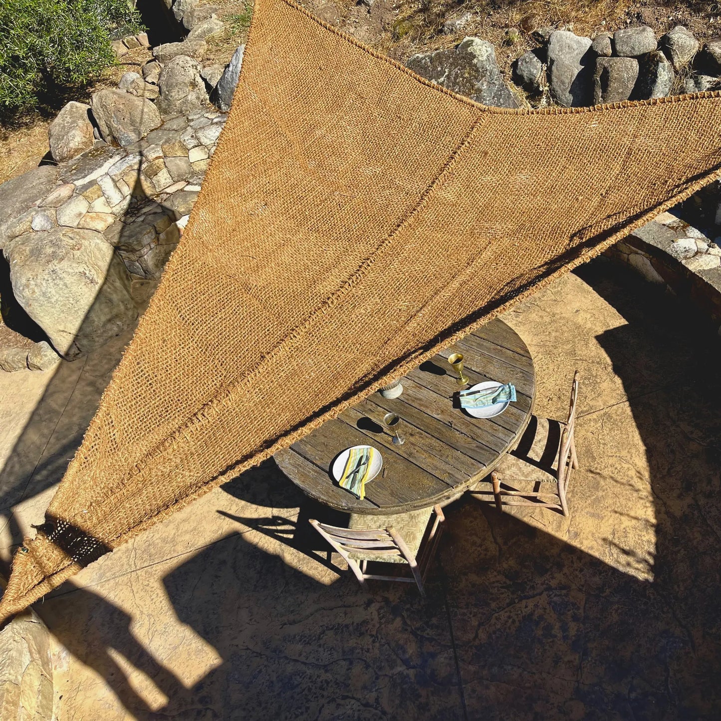 Handwoven fibre made from coconut fibre breathable sunshade over a wooden table with drinks on a stone patio rustic european