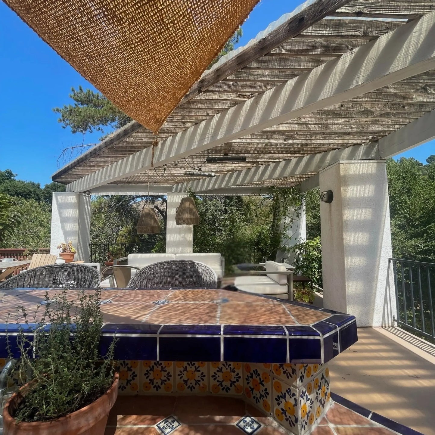Outdoor patio with a tiled table, chairs, and a pergola under a clear blue sky. 12' x 12' x 12' triangle coconut fibre shade sail natural fibers handmade artisan spanish rustic vibes non toxic 