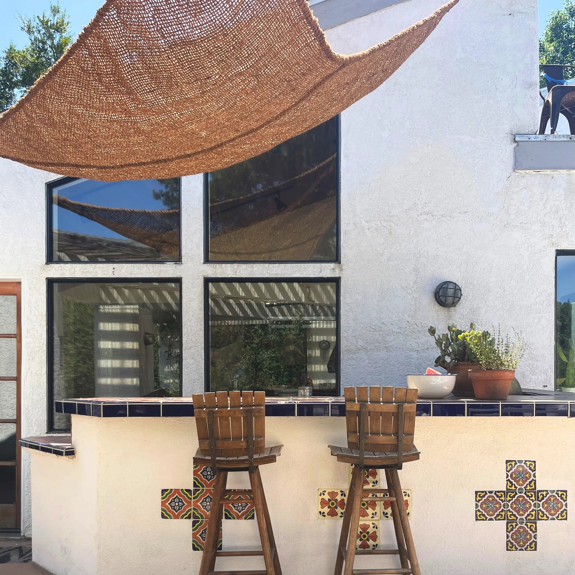Outdoor patio area with wooden stools, decorative tiles, and a woven canopy. 12' x 12' x 12' triangle coconut fibre shade sail natural fibers handmade artisan spanish rustic vibes non toxic coco du sol chic living happy hour bar