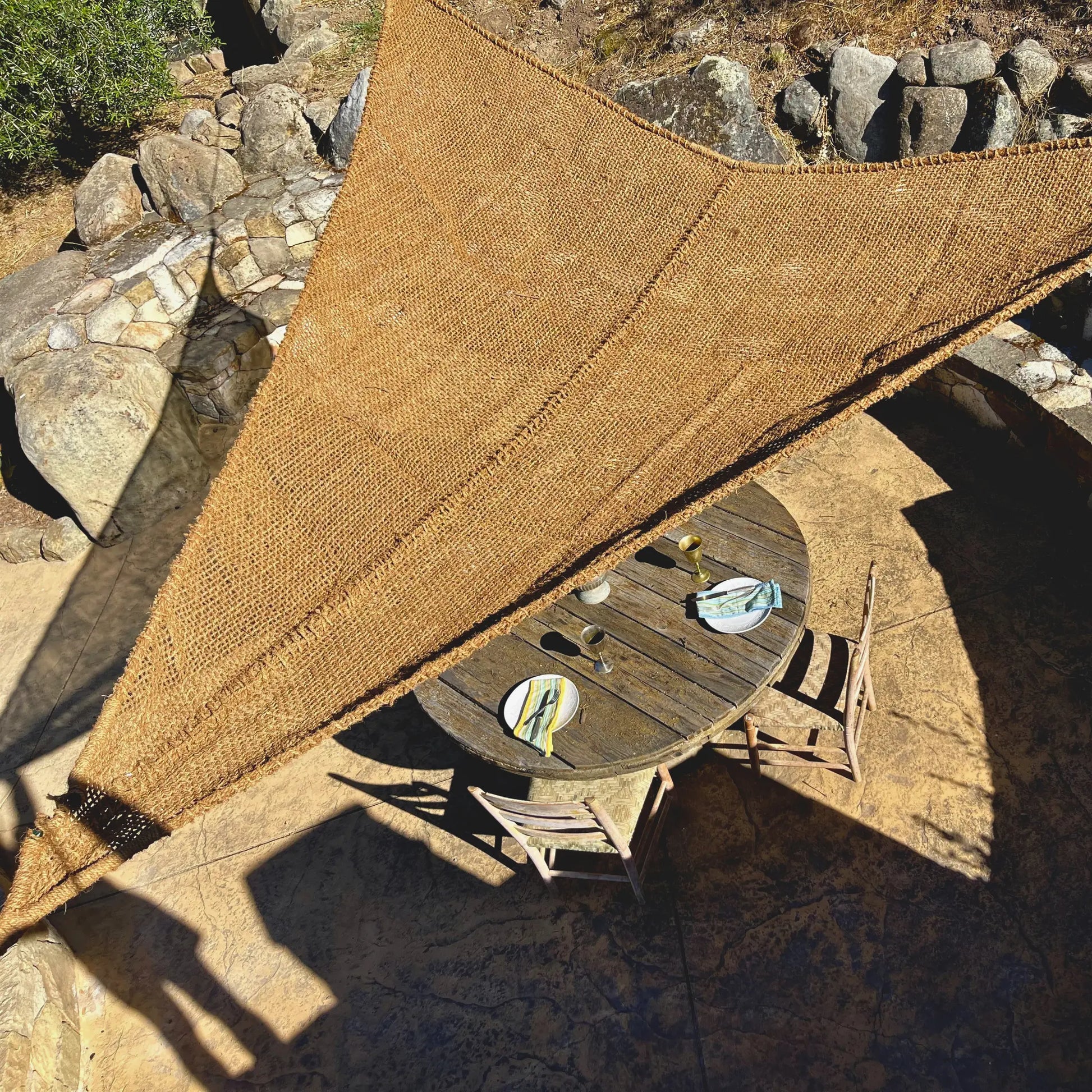 Handwoven fibre made from coconut fibre breathable sunshade over a wooden table with drinks on a stone patio rustic european