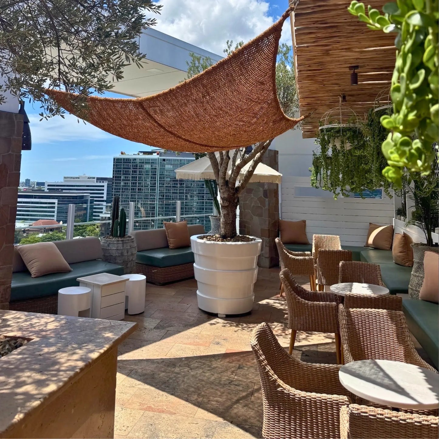 Outdoor patio area with furniture, plants, and city skyline view. 12' x 12' x 12' triangle coconut fibre shade sail natural fibers handmade artisan europe rustic vibes non toxic rooftop bar Australia Brisbane coco du sol filtered dappled light breathable shade pattens 